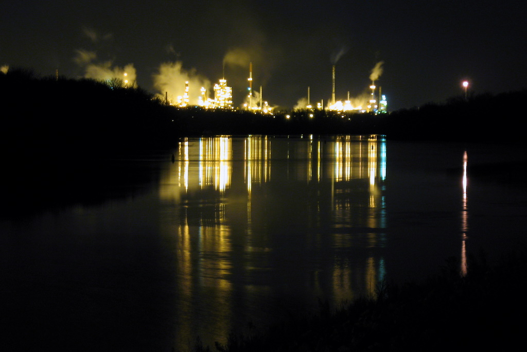 Night time photograph of the Ashland Oil plant in Newport with streaks of lights on the Mississippi River waters